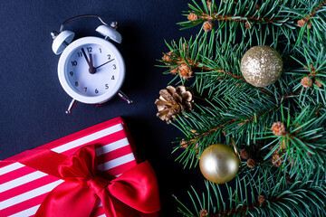 Christmas background: fir-tree branches, clock, gift on a black background.