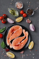 Fresh raw salmon steaks on a grill pan and ingredients on a dark background. Top view. Vertical format