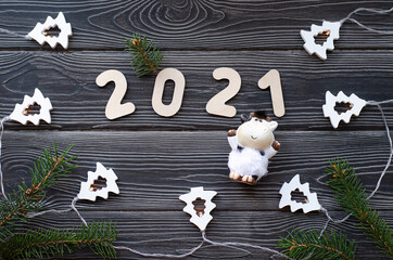 Christmas tree branches with a garland and the number 2021 on a dark wooden background. Bull-symbol of the new year 2021.