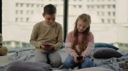 Children sitting on floor with cell phones. Siblings playing mobile games.