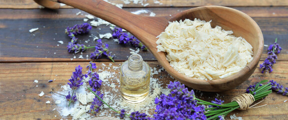 spoon full of flakes of soap with essential oil and lavender flowers on wooden background