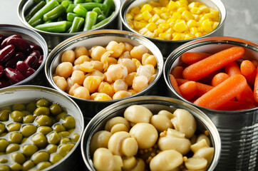 Canned vegetables in opened tin cans on kitchen table. Non-perishable long shelf life foods background