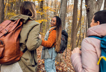 Three female friends having fun and enjoying hiking in forest on a beautiful autumn day.
