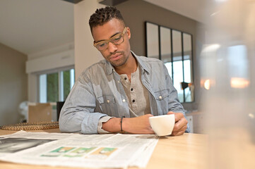 Handsmone cheerful guy reading newspaper and having coffee at home