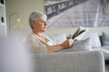 Senior woman reading newspaper, relaxed in sofa