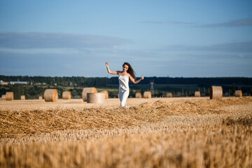 Young curly-haired woman in a wheat field, where there is a huge sheaf of hay, enjoying nature. People and travel. Nature. sun rays Agriculture