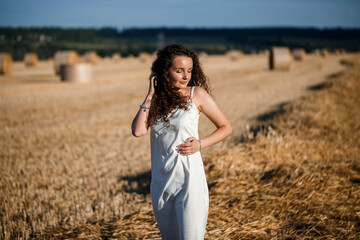 Young curly-haired woman in a wheat field, where there is a huge sheaf of hay, enjoying nature. People and travel. Nature. sun rays Agriculture