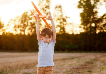 Happy child runs with a toy airplane on a sunset background over a field. The concept of a happy family. Childhood dreams.