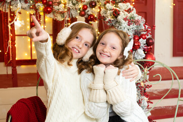 Fototapeta na wymiar two red-haired sisters on the veranda of a house decorated for Christmas. to point with a finger.