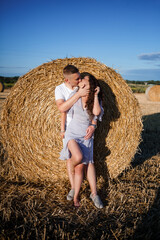 Attractive woman posing in the mown wheat fields with a sheaf in the village. Hay bales on the field after harvest, a place for a photo session of a beautiful Slavic couple