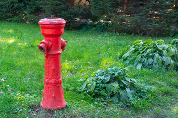 Old fire hydrant of red color on the green grass of the lawn. Fire safety concept. Selective focus, close-up