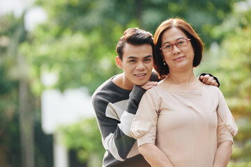 Obraz premium Portrait of happy pretty mature Vietnamee woman and son hugging her from behind