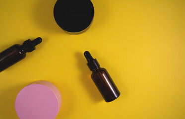 Cosmetic containers: jar of cream and bottle of serum on yellow background. Flat lay, top view and copy space