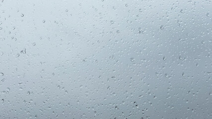 Cloudy weather and rain outside the window. Drops on glass on a gray and white background.