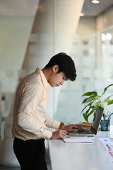 Side view of businessman is standing at his workstation and working wih computer laptop in modern office.