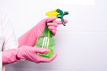 female hand in a rubber glove holding a spray for cleaning surfaces