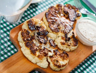 Vegetarian concept. Broiled cauliflower served on wooden board with sauce