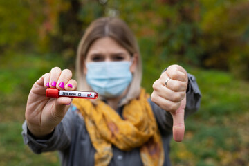 Young caucasian woman with mask is holding a test tube with blood sample, having covid-19 symptoms