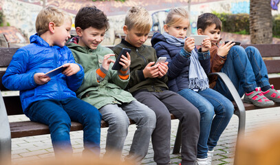 Group of children carried away with phone spending time together outdoors in autumn day