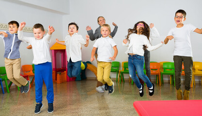 Positive happy smiling female teacher and group of schoolkids jumping in classroom