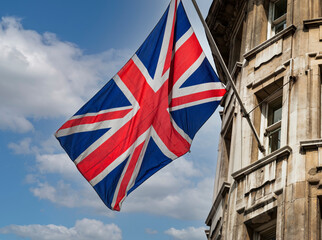 Fototapeta na wymiar UK flag waving on a building on blue sky background with white clouds.