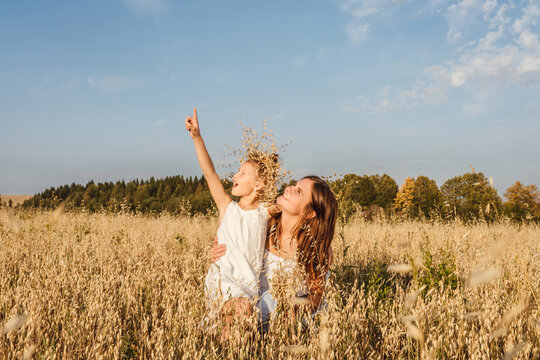 Beautiful young mother and her daughter look up and show with finger to sky. White clothes, freedom concept. Copy space, fromt view.