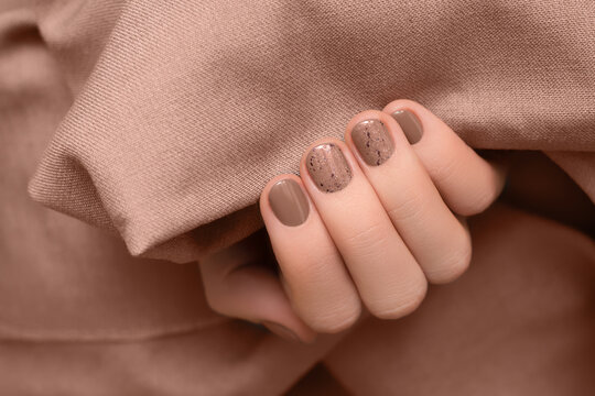 Female hand with brown nail design. Brown nail polish manicure. Woman hand on brown fabric background