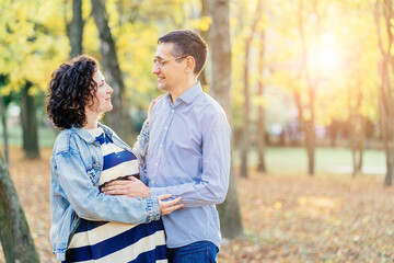 Happy parents, mom and dad, hugging baby bump, enjoying beautiful moment at park. Young family or couple or man and pregnant woman walking through colorful trees in fall or autumn.