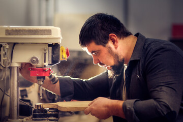 Bearded kraft caucasian man in a carpentry workshop with a drilling machine handcrafted wood board, concept handicraft and craftsmanship close up