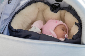 Three month old baby girl lying outside in a fleece jacket and pram.