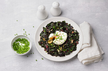 Braised chard with garlic and poached egg, seasoned with spices and green onions on gray background, top view. delicious healthy breakfast	