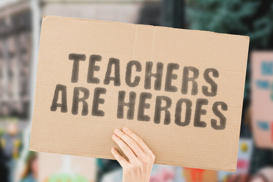 The phrase " Teachers are heroes
 " on a banner in men's hand with blurred background. Education. Studying. Job. Profession. Important. Essential workers