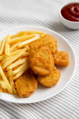 Tasty Fastfood: Chicken Nuggets and French Fries on a plate on cloth, side view.