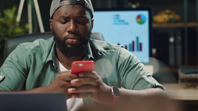 Closeup young african american man typing message on mobile phone in hipster office