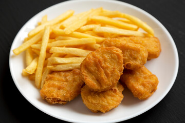 Tasty Fastfood: Chicken Nuggets and French Fries on a plate on a black background, side view.