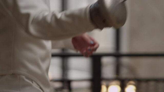 Close-up slow motion hands of fencer in a white suit hold a sword and compete with an unidentified opponent. Concept of Sports Fencing