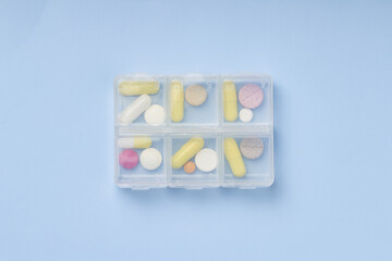 Dose pill box with medical pills on blue background. Top view. Flat lay.