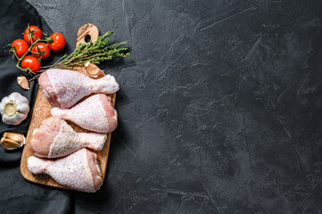 Raw fresh chicken drumsticks with spices and vegetables on a wooden cutting board. Black background. Top view. Copy space