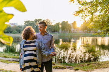 Pregnant woman in striped dress with husband walking in summer park. Mother and father. Happy parents. Autumn family portrait. Pregnancy, maternity, expectation concept.