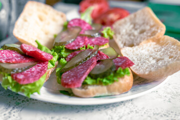 Preparing sandwiches with salami, tomato, pickles and lettuce