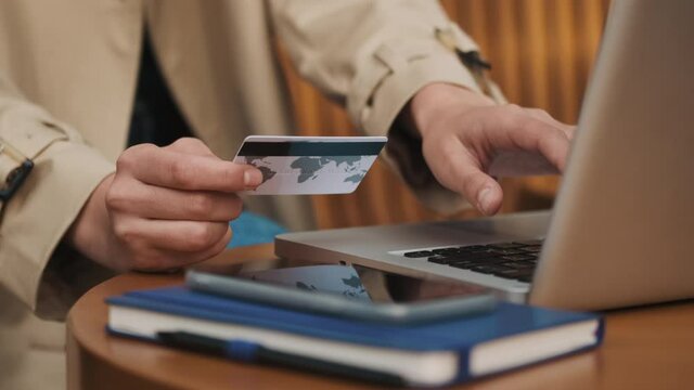 Close up shot of pretty student girl typing on laptop paying online by credit card resting in cafe outdoor