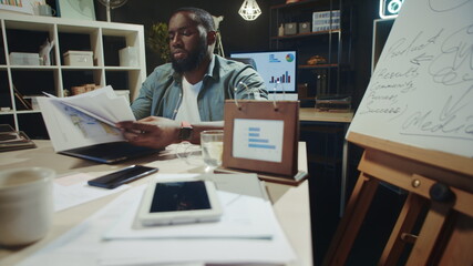 Focused african man reading documents in late office. Afro guy working overtime