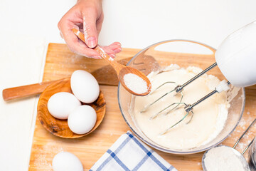 making dough for bread or homemade baked goods. ingredients on the desk. female hands hold a mixer for mixing dough