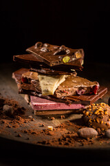 Stack of assorted chocolate with cocoa and cocoa beans on black background