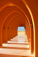 Fototapeta na wymiar Colorful orange arched hallway passage with columns leading to a desert on a sunny day.