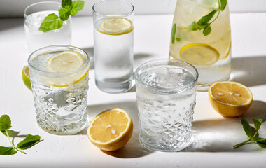 drink, detox and diet concept - glasses with fruit water or lemonade, lemons, limes and peppermint on white table
