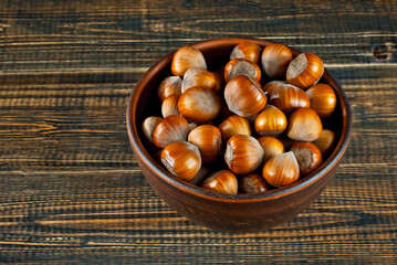 Hazelnuts in a bowl on a brown wooden background. Lots of nuts on an old shabby board. Place for text and copy space near food.