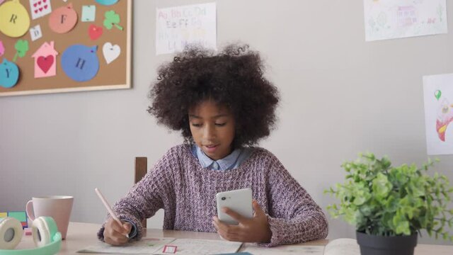 African american child kid school girl holding phone distance learning class using mobile application, watching online tutoring lesson, video calling in app virtual studying at home, in classroom.