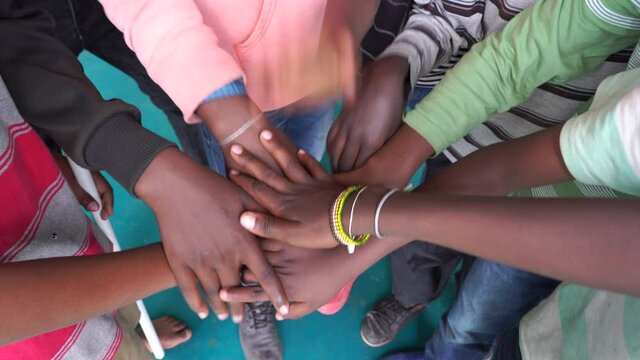 Arm stacked together one by one in unity and teamwork. Many hands getting together in the center of a circle. Close up outdoor shot. Many african children hands connecting, Tanzania, East Africa
