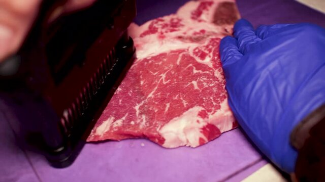 A close up shot of a raw beef steak being tenderized with a hand held kitchen tool meant for tenderizing meat.